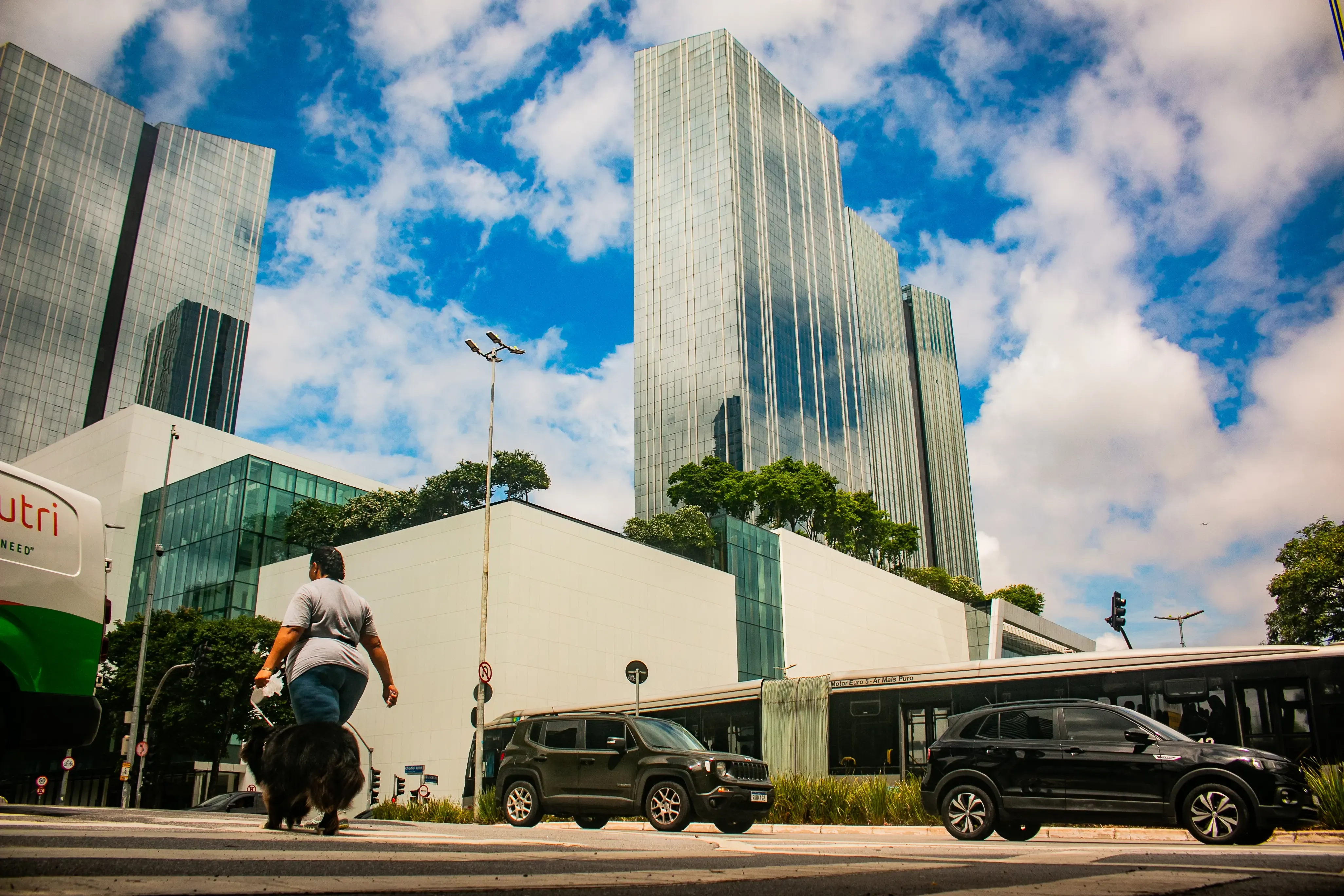 Pedestrian crossing in front of glass towers with cars and a bus at street level