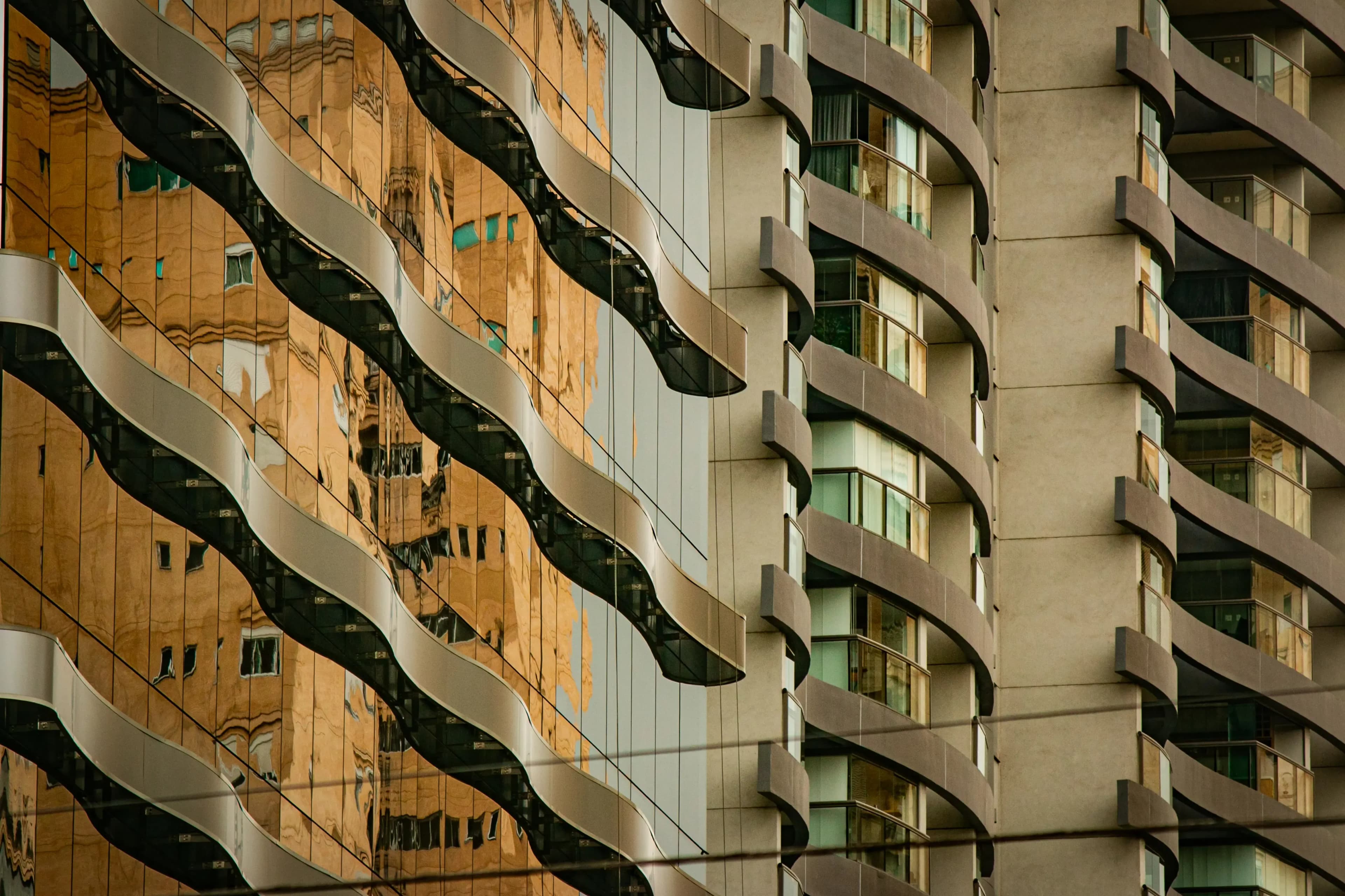 Architectural detail of wavy mirrored and concrete high-rise facades reflecting neighboring buildings