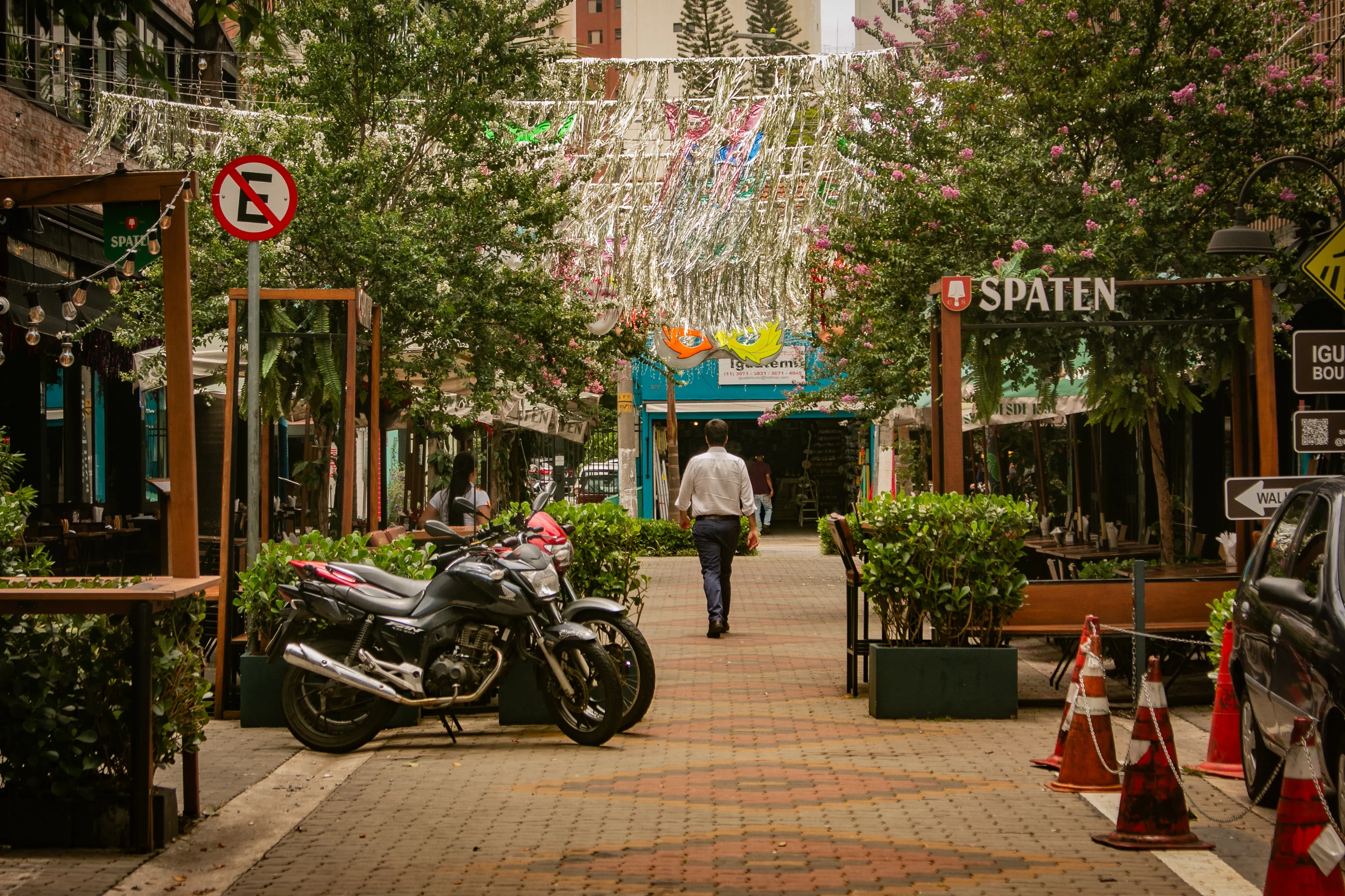 Pedestrian lane with outdoor restaurants, parked motorcycles, and a man walking ahead