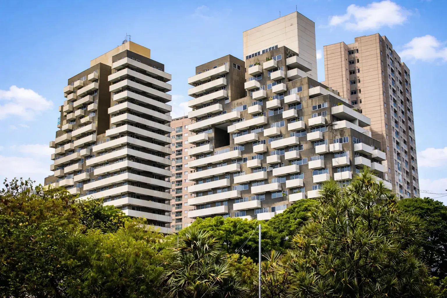 Cluster of modern apartment towers rising above a dense canopy of trees